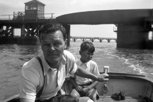 A small outboard motor boat entering Langstone Harbour havimg passed under the railway swing bridge which frames a view of the 1824 road bridge and its swing section. Roger Nash